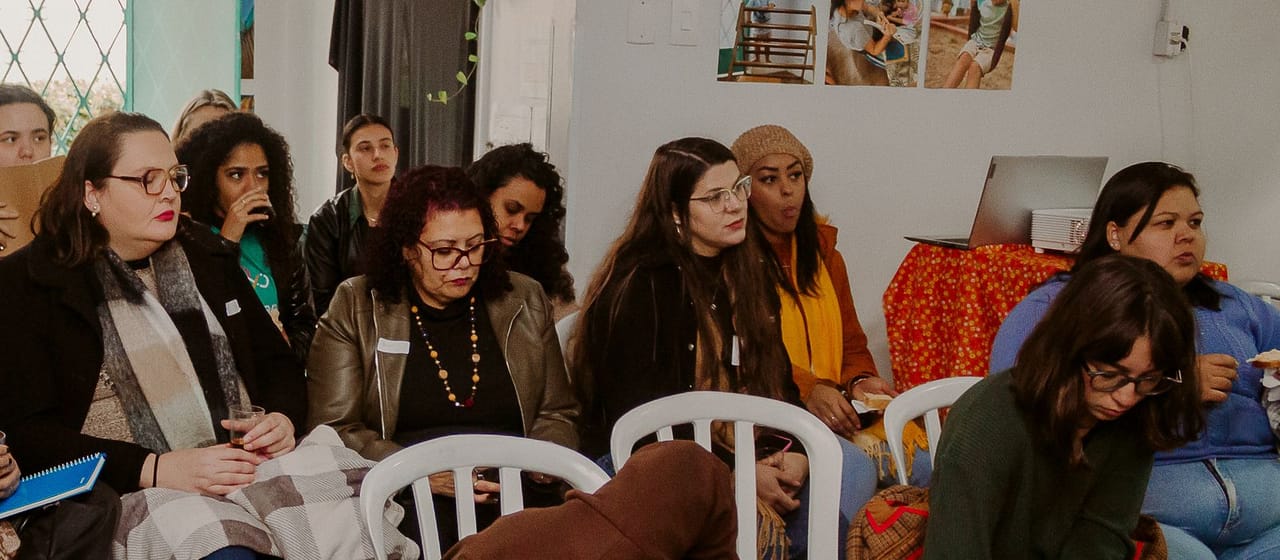 Participantes de uma formação do coletivo, sentadas em roda, acompanhando a apresentação